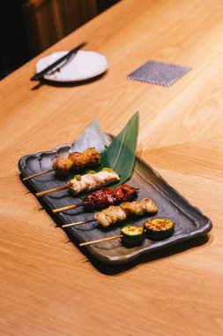 Yakitori (Japon Usulü Izgara Tavuk Şişler) tavuk, iç organ ve salatalık siyah taş plaka üzerinde servis.