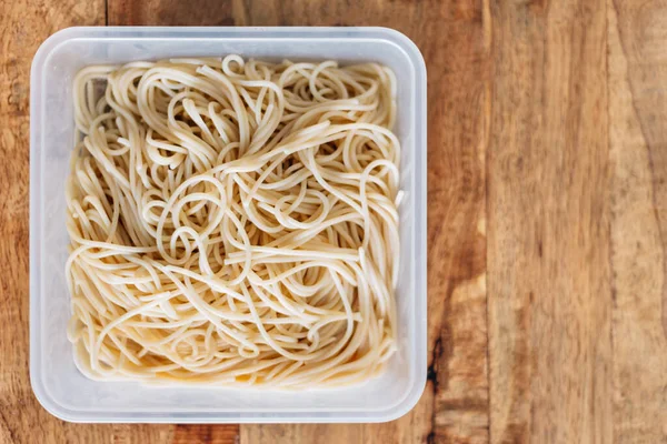 Top view of boiled spaghetti pasta in plastic box on wooden table. Cooking at home. Start and promote your food business.