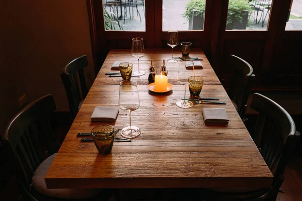 Fine dining wooden table with cutleries, wine glasses, napkins and naperies with lighted candle on the table. Light source from window light.