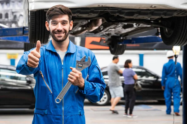 機械的な親指を立って 背景にブラーガレージとレンチを保持します 自動車修理サービスセンター 専門職 — ストック写真