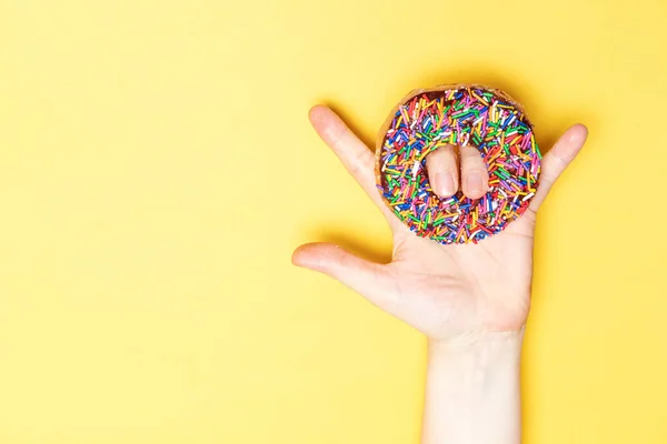 I love you hand sign with chocolate frosted donut with sprinkles, sugar-glazed frosted on yellow background. Playful and joyful tasty sugary comfort food for customer with copy space. Donut lovers.