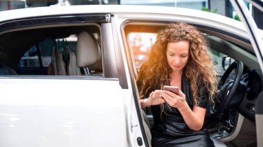 Kafkasyalı kadın arabada oturuyor ve akıllı telefonuna bakıyor. Otomobil Uygulaması. Oto kiralama işi. Dijital İş. 