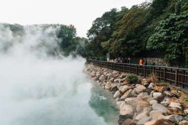 Beitou Parkı 'ndaki ünlü Beitou Termal Vadisi' nde, Tayvan 'ın Taipei şehrindeki ağaçların arasından süzülen sıcak kaynak kaynayan buharı ile turist seyahati.