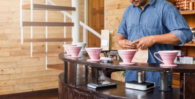 Erkek barista, damlatma adı verilen alternatif bir yöntemle kahve yapıyor. Kahve öğütücüsü, kahve standı ve ahşap tezgahın üzerine dökülmüş..