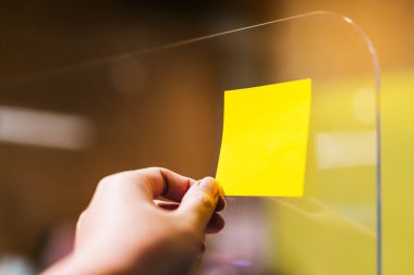 İş adamları fikir paylaşımı ve planlama konusunda fikir alışverişinde bulunmak için pleksiglas ayırıcılara yapışkan notlar yazıyorlar. Covid-19 sırasında ofisteki sosyal mesafeler için yeni normal kavram.