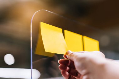 İş adamları fikir paylaşımı ve planlama konusunda fikir alışverişinde bulunmak için pleksiglas ayırıcılar üzerinde yapışkan notlar kullanıyorlar. Covid-19 sırasında ofisteki sosyal mesafeler için yeni normal kavram.