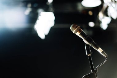Kablolu yayına bağlanan mikrofon stüdyodaki ışığın bulanıklığı ile konferans salonu ışığı ya da podcast kaydı konuşuluyor. Olay Arkaplanı. Uzayı sola kopyala.