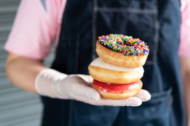 Çikolata kaplı donut serpiştirme, şeker kaplı krema ve lateks eldiven takan kadın elinin üstüne Bavyera çöreği. Neşeli ve neşeli müşteriler için lezzetli, şekerli ve rahatlatıcı yemekler..