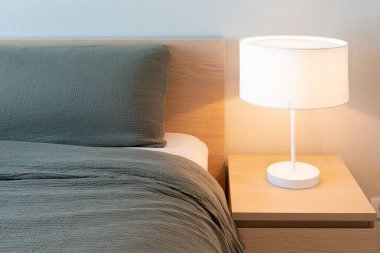 Gri battaniyeli yatak ve yastıklı beyaz lamba yatak odasının iç tarafındaki masanın üzerinde. Minimalist konfor yatak odası tasarımı günlük yaşam için. Uzayı kopyala, yatay. Gerçek resim.