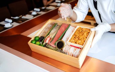 Şef, mavi yüzgeçli ton balığı (Toro ve Chutoro), uni, çiğ karides, trüf mantarı, wasabi ve havyar gibi omakaz yemeğini yapmadan önce ahşap bir kutuda özel taze malzemeler sunar..