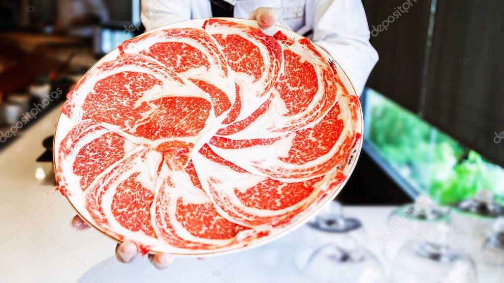 The chef presents Premium Rare Slices Kagoshima Wagyu A5 beef with a high-marbled texture on a circle plate served for Omakase meal. Premium ingredient.