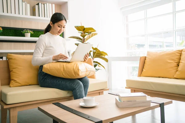 Asian woman sitting and working on the sofa. Business woman working on laptop at home. Woman working in a relax area in the office. Business quarantine period.