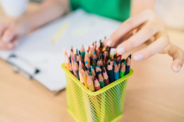 The child's hand picks up the colored pencils in a small box to continue coloring in the work. Children's creativity expressed through art in kindergarten and elementary school. back to school.