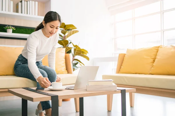 Asian woman sitting and working on the sofa. Business woman working on laptop at home. Woman working in a relax area in the office. Business quarantine period.