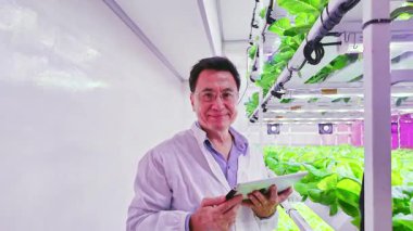 Laboratuvar önlüklü bilim adamı LED ışıkları altında hidrofonik dikey çiftliği izlemek için tablet kullanıyor. Kapalı alanda tarım teknolojisi, tarım, bahçıvanlık ve tarım alanındaki modern tarımı gösteriyor..