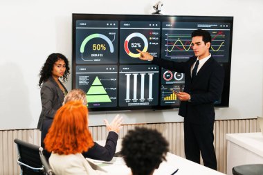 Konferans odasındaki iş ekibi sunucu stratejiyi dijital gösterge paneliyle açıklıyor. Toplantıda grafikler, grafikler, veriler, analitik, istatistik ve odaklanmış bir sunum oturumu yer alıyor.