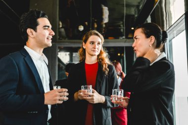 Kurumsal resepsiyonda resmi giyinen üç profesyonel içkilerle sohbet ediyor. Etkinlik sahnesinde satışlar, ortaklık, seminer atmosferi, işbirliği, planlama ve yeni fırsatlar yer alıyor.