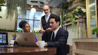 İki profesyonel modern bir kafede buluşup bir sunucu siparişlerini alırken laptopun başında iş tartışıyorlar. Kahve fincanları, yeşillik ve doğal ışık rahat ama verimli bir iş ortamı yaratır..