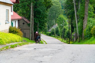 Yaz aylarında küçük bir kasaba yolu boyunca bisiklet iterek yaşlı bir kadının arka görünümü