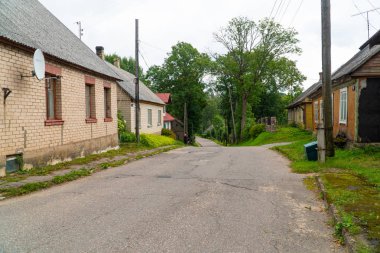 Yaz aylarında küçük bir kasaba yolu boyunca bisiklet iterek yaşlı bir kadının arka görünümü