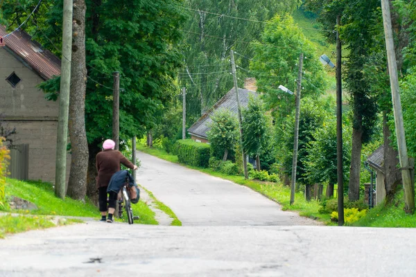 Yaz aylarında küçük bir kasaba yolu boyunca bisiklet iterek yaşlı bir kadının arka görünümü