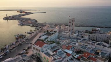 Eski Katedral San Corrado (Duomo Vecchio) ile Molfetta rıhtımında uçan İHA 'dan güzel panoramik 4K video, gemi ve yatlı liman ve Molfetta şehir günbatımı. Apulia, İtalya