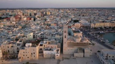 Eski Katedral San Corrado (Duomo Vecchio) ile Molfetta rıhtımında uçan İHA 'dan güzel panoramik 4K video, gemi ve yatlı liman ve Molfetta şehir günbatımı. Apulia, İtalya