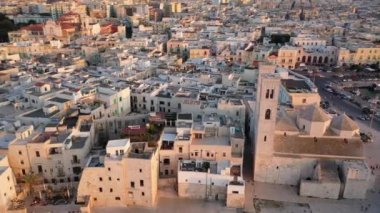 Eski Katedral San Corrado (Duomo Vecchio) ile Molfetta rıhtımında uçan İHA 'dan güzel panoramik 4K video, gemi ve yatlı liman ve Molfetta şehir günbatımı. Apulia, İtalya