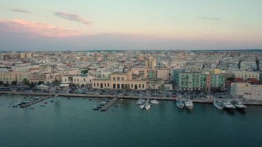 Eski Katedral San Corrado (Duomo Vecchio) ile Molfetta rıhtımında uçan İHA 'dan güzel panoramik 4K video, gemi ve yatlı liman ve Molfetta şehir günbatımı. Apulia, İtalya