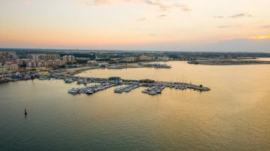 Molfetta limanındaki deniz fenerinde uçan İHA 'dan güzel panoramik hava manzaralı fotoğraf. Günbatımında gemiler, liman, yat kumu ve Molfetta şehriyle arka planda.)