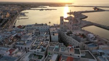 Eski Katedral San Corrado (Duomo Vecchio) ile Molfetta rıhtımında uçan İHA 'dan güzel panoramik 4K video, gemi ve yatlı liman ve Molfetta şehir günbatımı. Apulia, İtalya