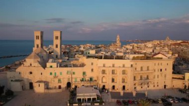 Eski Katedral San Corrado (Duomo Vecchio) ile Molfetta rıhtımında uçan İHA 'dan güzel panoramik 4K video, gemi ve yatlı liman ve Molfetta şehir günbatımı. Apulia, İtalya