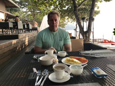 Bir adam açık hava restoranında oturuyor ve kahvaltı yapıyor.