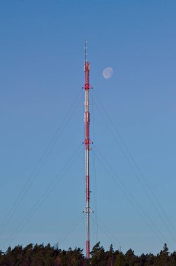 Gündüz yüksek kırmızı ve beyaz hücre kulesi, kulenin tepesinde ay parlıyor..