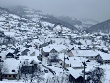 Dağlar ve ağaçlarla kaplı kış manzarası, Romanya Transilvanya 'nın kırsal karlarına ev sahipliği yapan köy.