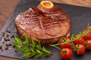 Grilled beef steak with cherry tomatoes and spices on black stone board clipart