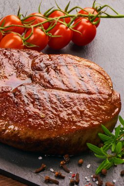 Siyah taş tahtada ızgara biftek, kiraz domatesleri ve baharatlar.