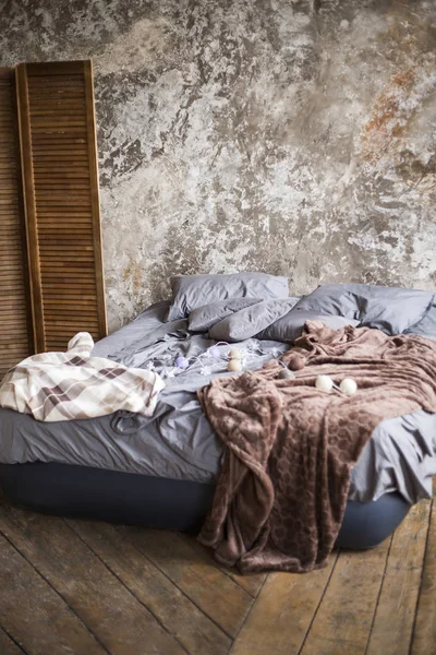 the air bed with gray bed linen and a brown cover on a wooden floor costs against the background of an impressive wall indoor.