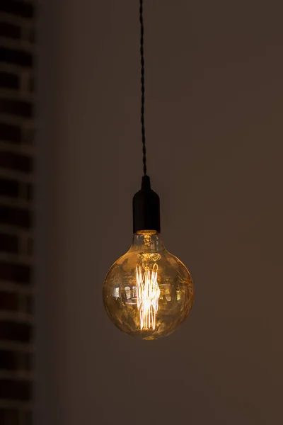 Solo lampadina appesa sullo sfondo di un muro. la lampadina brucia. Stanza oscura. una lampada con una presa nera — Foto Stock