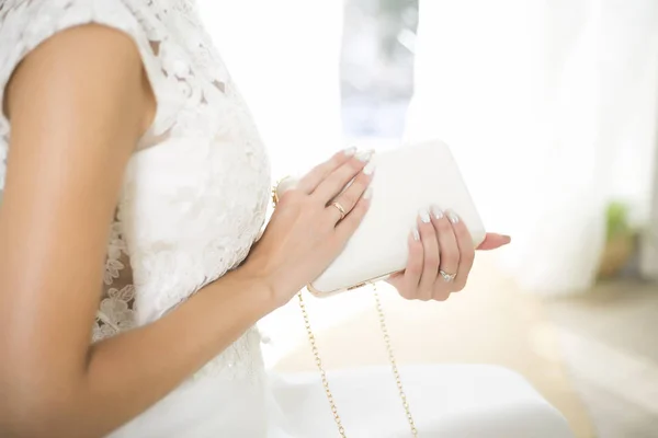 Menyasszony menyasszonyi ruhában tartja a kezében a fehér táskát. Gyönyörű manikűr. Esküvő napja. Jegygyűrűk — Stock Fotó