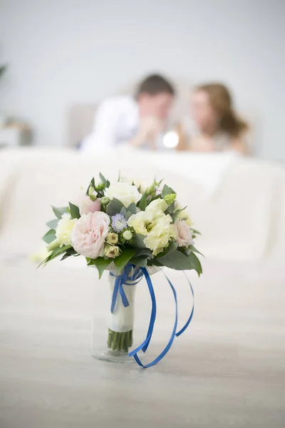 Bouquet de mariage de roses avec une bande bleue coûte dans un vase. Dans le contexte des jeunes mariés se trouvent sur un lit — Photo