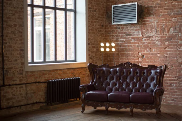 claret leather sofa to the loft an interior with a bright searchlight and a window. brick wall. ancient pig-iron battery