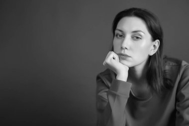 Düşünceli bir kadın karanlık bir stüdyoda oturur ve elini yüzüne tutar. siyah beyaz fotoğraf.