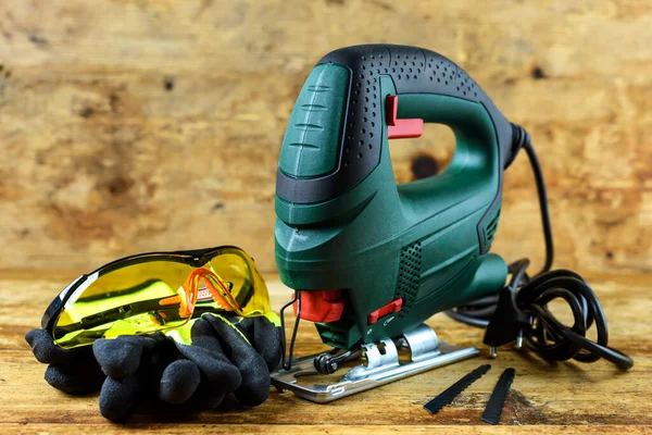 Eski ahşap arka planda elektrikli yapboz için bir yapboz, koruyucu gözlükler, eldivenler ve bıçaklar..