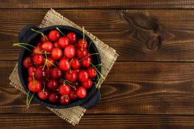 Koyu kahverengi ahşap bir masada siyah bir kasede kırmızı kirazlar ve metin için fotokopi alanı. Üst görünüm.