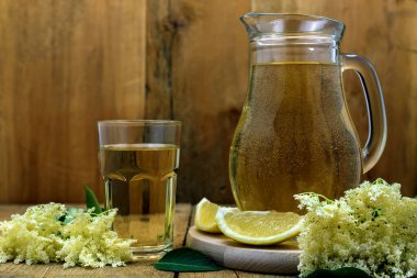 Eski ahşap masada limon ve yaşlı çiçekleriyle ev yapımı bir sürahi ev yapımı elderflower suyu. Seçici odak.