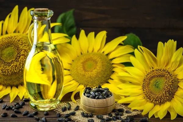 Sunflower oil in a bottle and sunflower seeds in bowl near fresh sunflower flower on a wooden table with copy space for text.