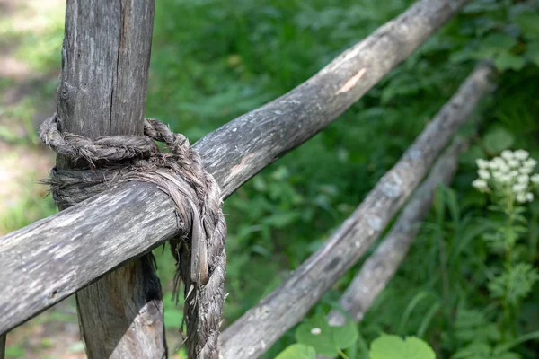 Knot bound wooden stick fence on a background of green grass. rope tied of old fence.  close up