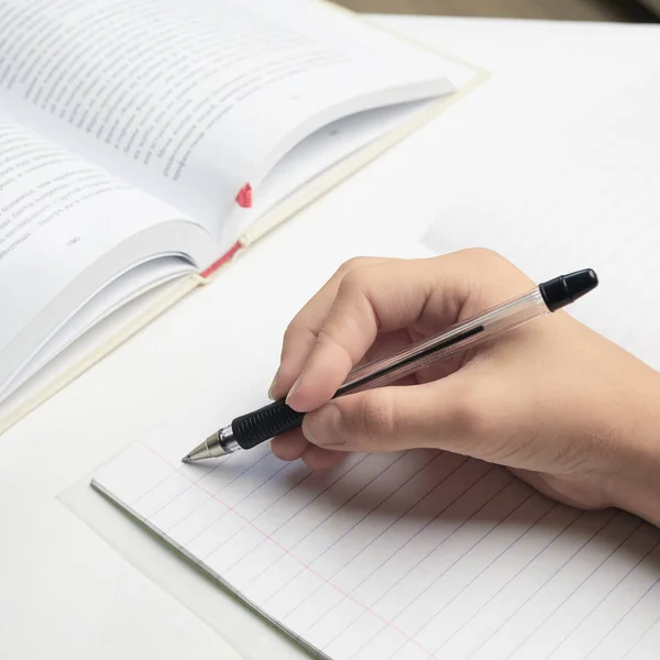 in the school lesson. hand holds a pen near a striped notebook. next to it is a book and a pencil. White background