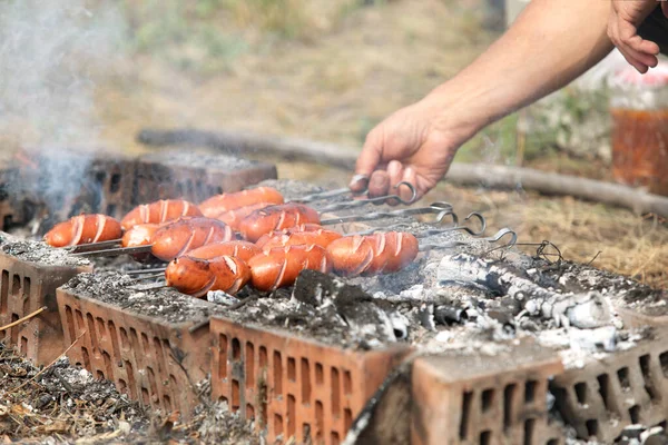 man\'s hand turns frying grill sausages on skewers on fire. Selective focus, visible smoke